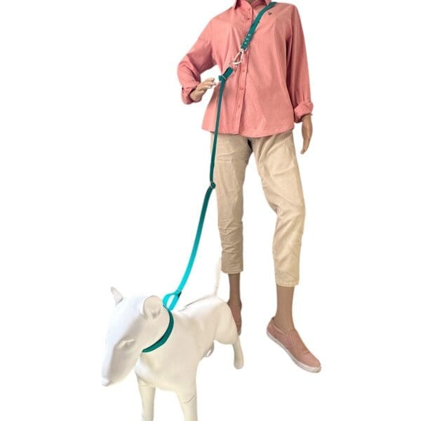A mannequin in a pink shirt, beige trousers, and pink slip-ons holds a teal WAVE 8-in-1 Hands-Free Waterproof Adjustable Dog Lead (2.5m, steel carabiner) attached to a white dog mannequin against a white background.