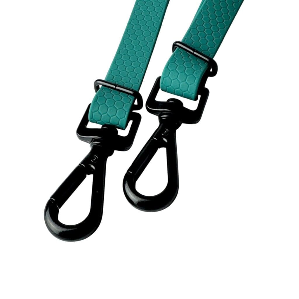 Two teal straps with a hexagonal texture and black metal swivel clasp hooks highlight the WAVE Hands-Free Lead, an adjustable and multifunctional dog lead, shown isolated on a white background.