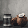 Screenshot 2025-05-24 at 13.57.46 A jar of Kiki Organic Raw Virgin Coconut Oil - 100% Raw is placed next to two brown coconuts, one split open to show the white coconut flesh, set against a gray background.