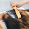 A hand uses the Truelove Bamboo Pet Shedding Comb to groom a pet’s thick, tri-colored (black, brown, and white) fur, effectively removing loose hair for cats or dogs.