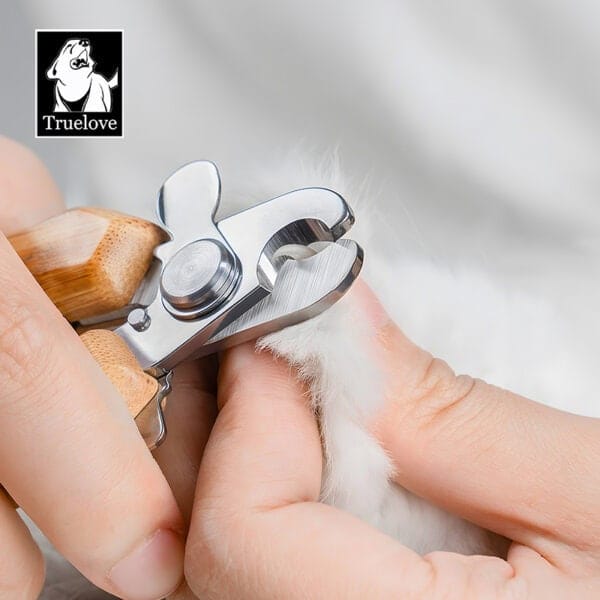 A close-up of someone trimming a fluffy white pet’s nails using the Bamboo Pet Nail Clipper with Safety Guard – Dog & Cat Grooming. The Truelove logo with a dog illustration is featured in the top left corner.