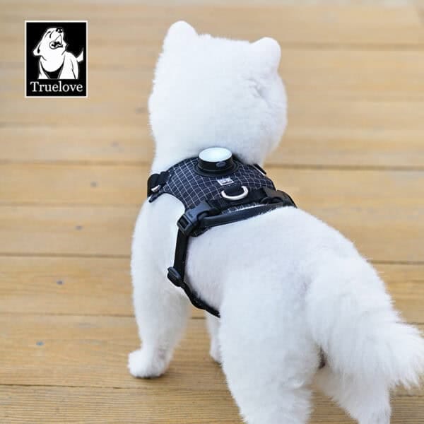 A fluffy white dog wears the Truelove TLH6771 LED Dog Harness - GPS Tracker Smart Safety on a wooden floor, facing away. The harness has a small round device and the Truelove logo with dog graphic is in the top left corner.
