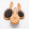 Three wooden hairbrushes with metal bristles are arranged on a white background, with one brush in the front and two slightly behind it, all featuring black cushioned bases.