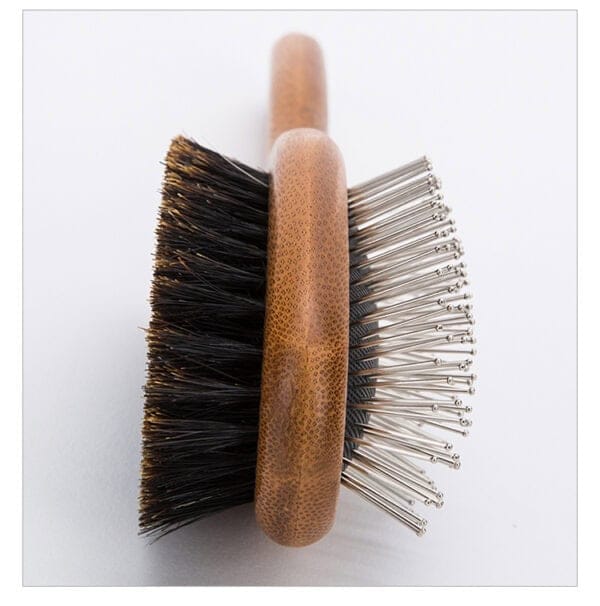Truelove Bamboo Pet Brush with Boar Bristles - angle A close-up of the Truelove Bamboo Pet Brush rests on a white surface, showing its wooden handle, black boar bristles on one side, and stainless steel pins with rounded tips on the other.