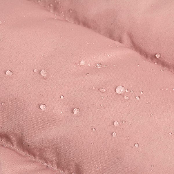 Close-up of the waterproof pink fabric with water droplets on the dog jacket, demonstrating its water-resistant quality for rainy conditions.