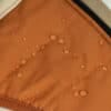 Water-resistant material of the Luxury Winter Dog Coat in orange showing water droplets on the surface, demonstrating the coat's durability in wet conditions.