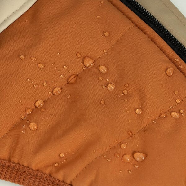 Water-resistant material of the Luxury Winter Dog Coat in orange showing water droplets on the surface, demonstrating the coat's durability in wet conditions.