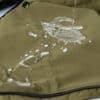 A close-up of the green windproof dog jacket, demonstrating its water-resistant fabric with water droplets rolling off.