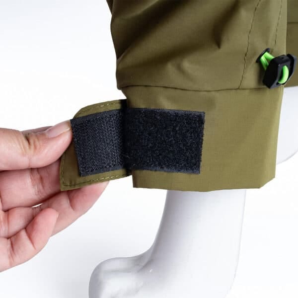 A close-up of the adjustable Velcro strap on the green windproof dog jacket, showing how it secures the fit.