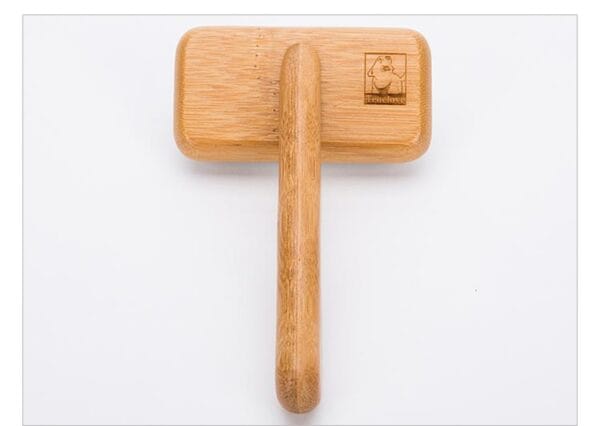 A Truelove Bamboo Pet Comb - Grooming Tool with a long handle and rectangular head, placed on a white surface. The head features an engraved logo of a chef's hat with the word "Travelbao.