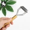 A hand holding the Truelove Bamboo Molting Hair Comb with a bamboo handle and metal blades. A green plant and the Truelove logo appear in the background.