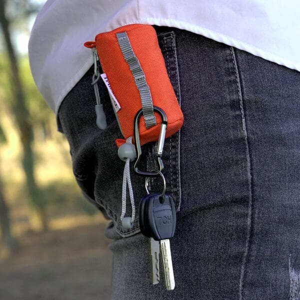 A small orange pouch with a zipper is clipped to a belt loop on dark jeans, next to two keys on a black keychain—ideal for carrying treats or accessories for the Truelove TLB2012 Waterproof Multi-Use Pet Carrier made with DuPont material.