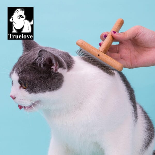 A person grooms a white and gray cat with the Truelove Bamboo Pet Comb - Grooming Tool against a light blue background. The Truelove logo, featuring a dog illustration, appears in the upper left corner.