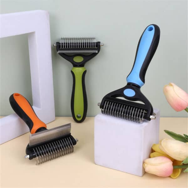 The 2 in 1 Pet Grooming Comb - Mats & Loose Hair Removal Brush, featuring ergonomic handles in orange, green, and blue, is displayed on white geometric blocks beside yellow and pink tulips against a light background.