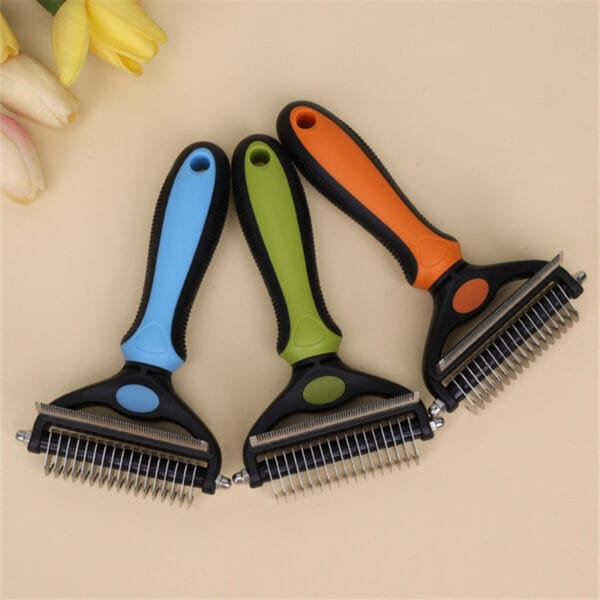 Three 2 in 1 Pet Grooming Combs for mats & loose hair, with black and blue, green, and orange handles, are arranged side by side on a light beige surface decorated with yellow and white flowers in the corner.