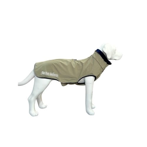 A mannequin dog wearing a light brown, fitted dog coat with black trim and "The Dogs Business" logo on the side, displayed on a plain white background.