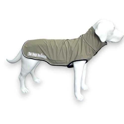 A white dog mannequin wearing a light brown, waterproof dog coat with black trim and the text "The Dogs Business" printed on the side. The background is plain white.