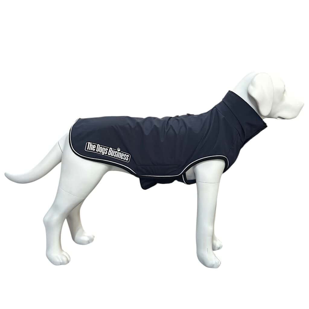 A white dog mannequin wears a dark blue dog coat with white trim and "The Dogs Business" logo on the side, displayed against a plain white background.