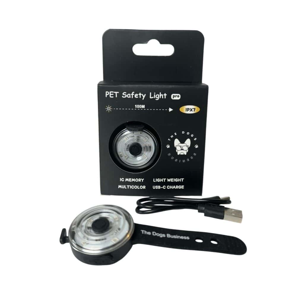 The Dogs Business Safety Light, along with a USB charging cable and black strap, is shown in front of its black packaging featuring text, symbols, and dog and cat illustrations.