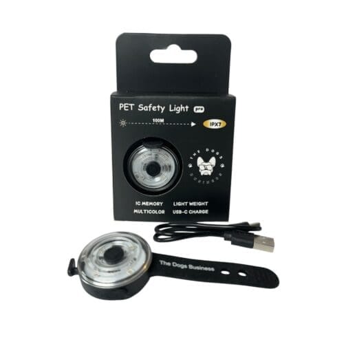 The Dogs Business Safety Light, along with a USB charging cable and black strap, is shown in front of its black packaging featuring text, symbols, and dog and cat illustrations.