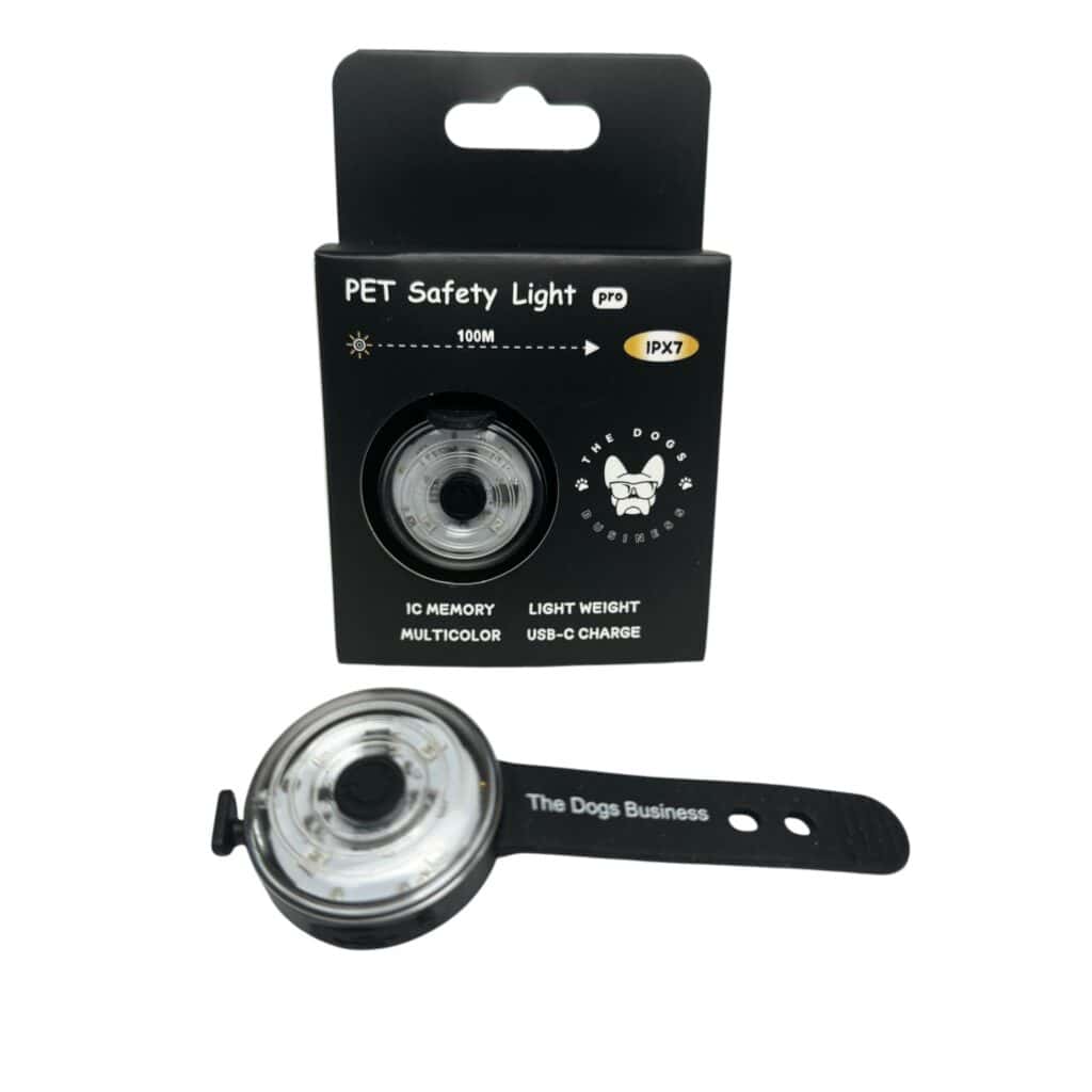 The Dogs Business Safety Light—a round, black and clear PET light with adjustable strap—is shown by its packaging featuring IC memory, multicolour options, lightweight build, USB charging, 100m range, and IPX7 waterproof rating.