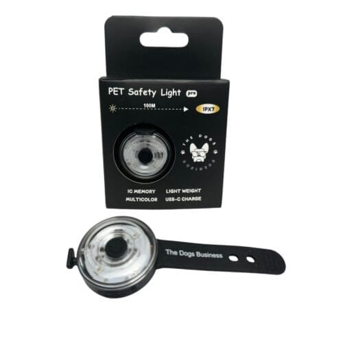 The Dogs Business Safety Light—a round, black and clear PET light with adjustable strap—is shown by its packaging featuring IC memory, multicolour options, lightweight build, USB charging, 100m range, and IPX7 waterproof rating.