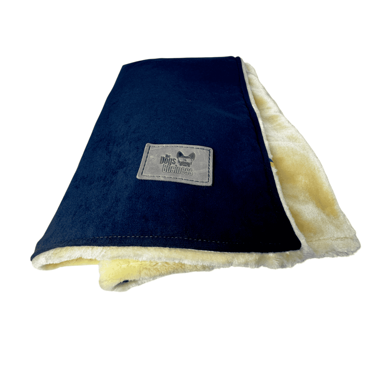 Velour Snuggle Blanket folded with a navy blue top, a cream-coloured plush underside, and a rectangular fabric patch labelled “The Dogs Business.”.