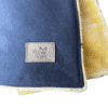Velour snuggle blanket in blue with a yellow faux-sheepskin lining and a rectangular patch featuring a logo of a French bulldog wearing sunglasses and the text “The Dog’s Business”.